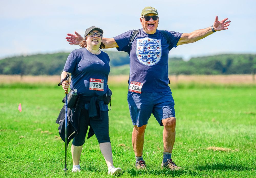 Two participants in matching England shirts celebrate at outdoor fun run event in sunny field.