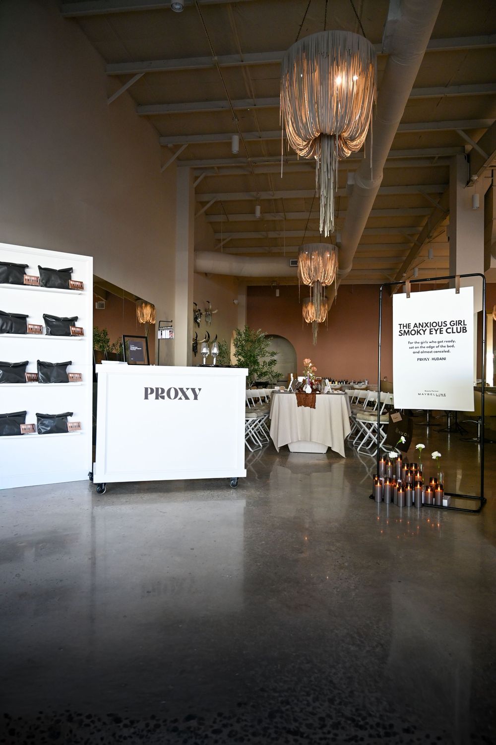 Elegant event space with a white PROXY display, chandelier lighting, candles, and The Anxious Girl Smoky Eye Club sign.