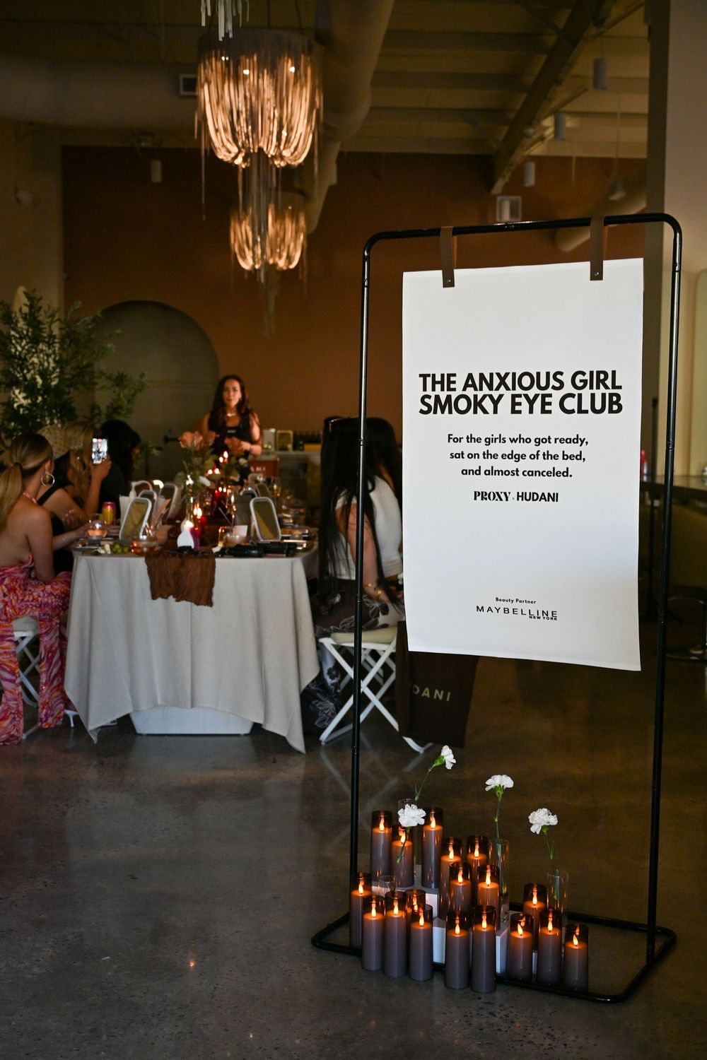 Maybelline Anxious Girl Smoky Eye Club event display with candles, white flowers, and guests at decorated tables.