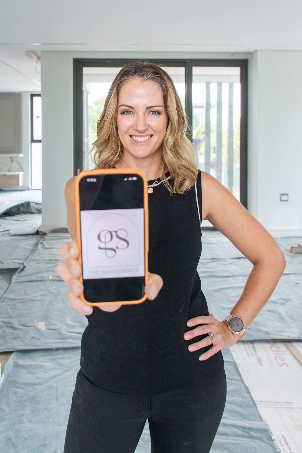 Lara, an interior designer in Johannesburg, holding phone displaying GS logo, standing in a renovated interior space.