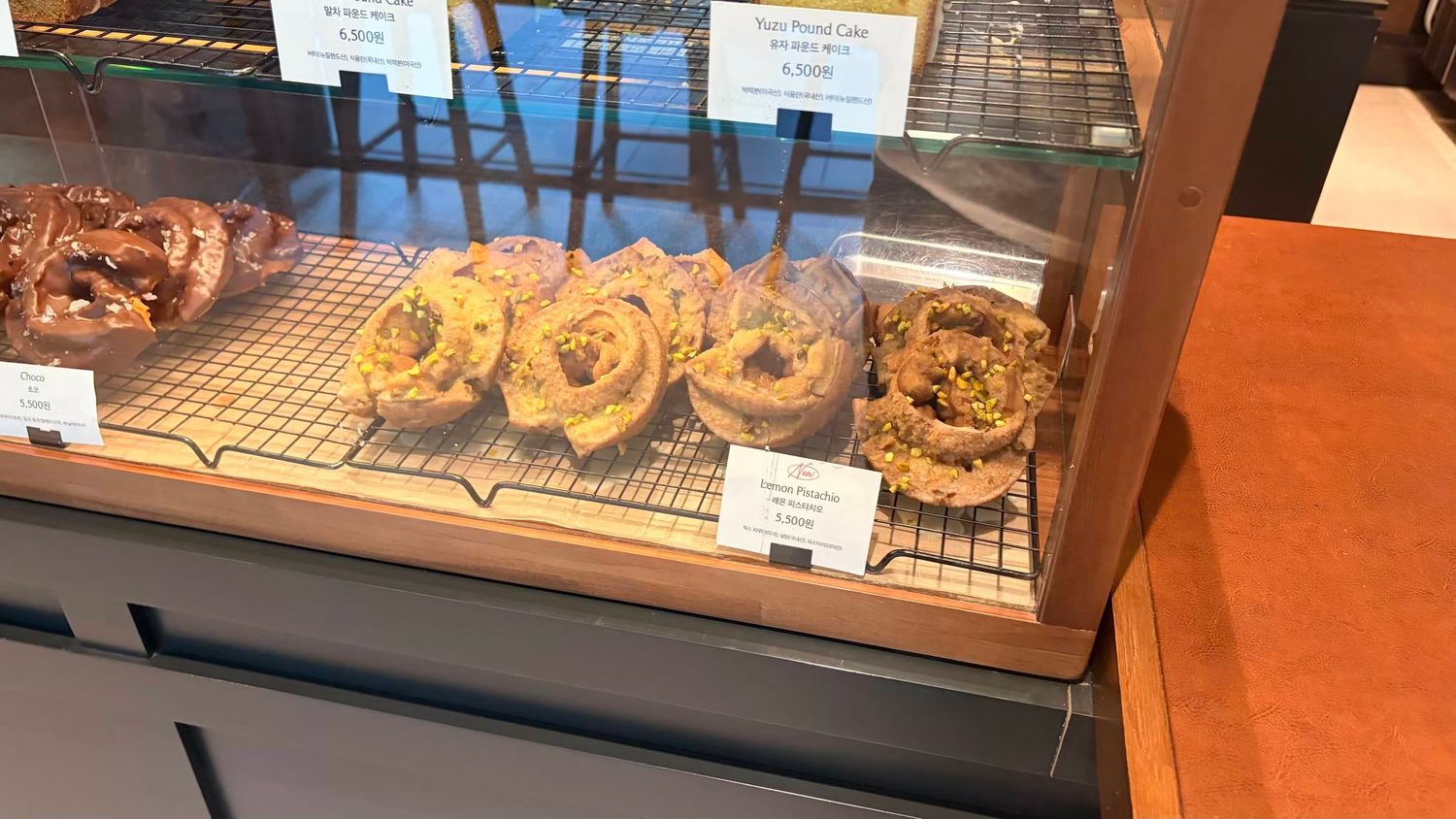 Glass bakery display case showcasing assorted frosted cronuts and pastries on wire cooling racks.