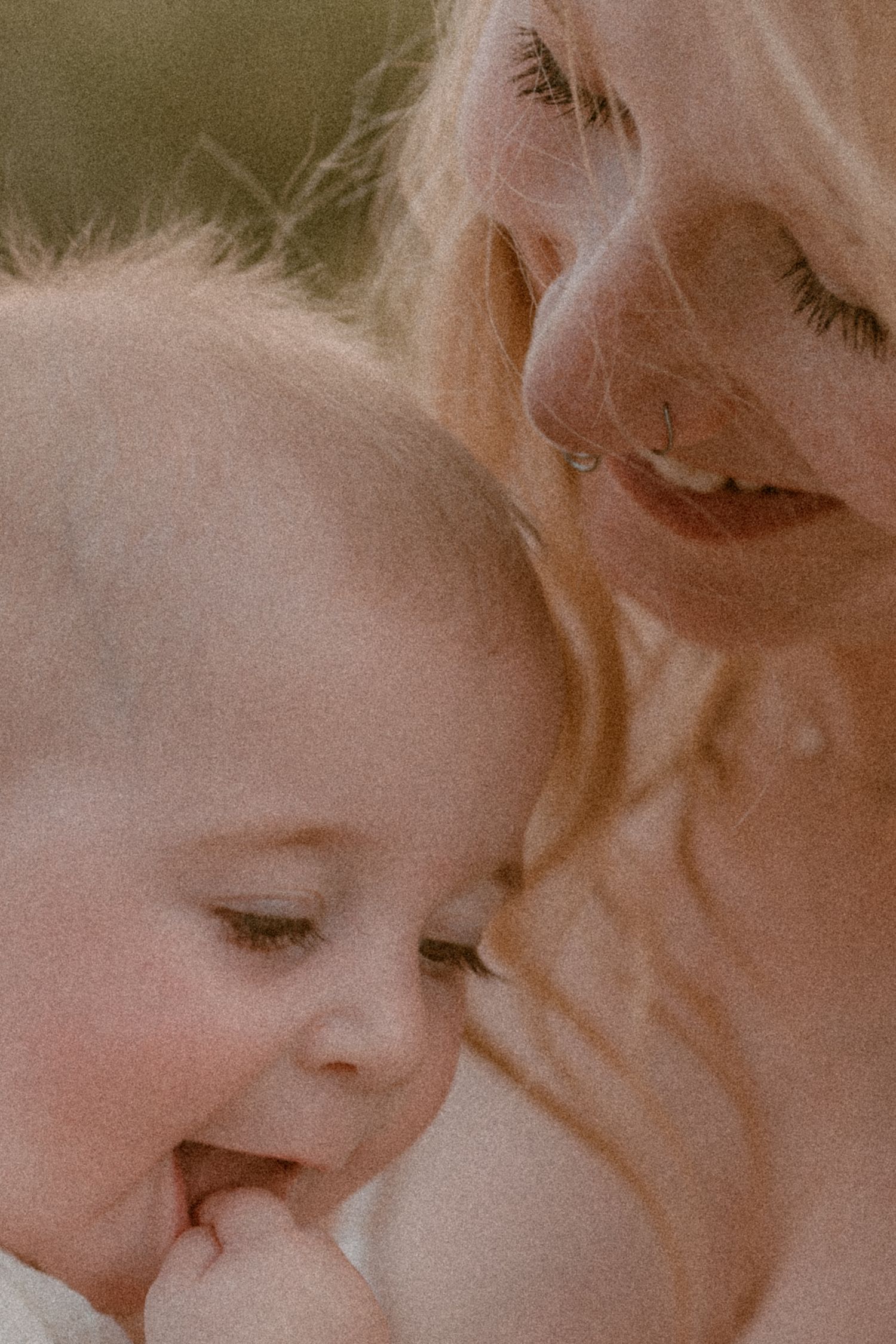 Close-up of a smiling mother with wavy blonde hair tenderly holding her baby, both sharing a peaceful moment.