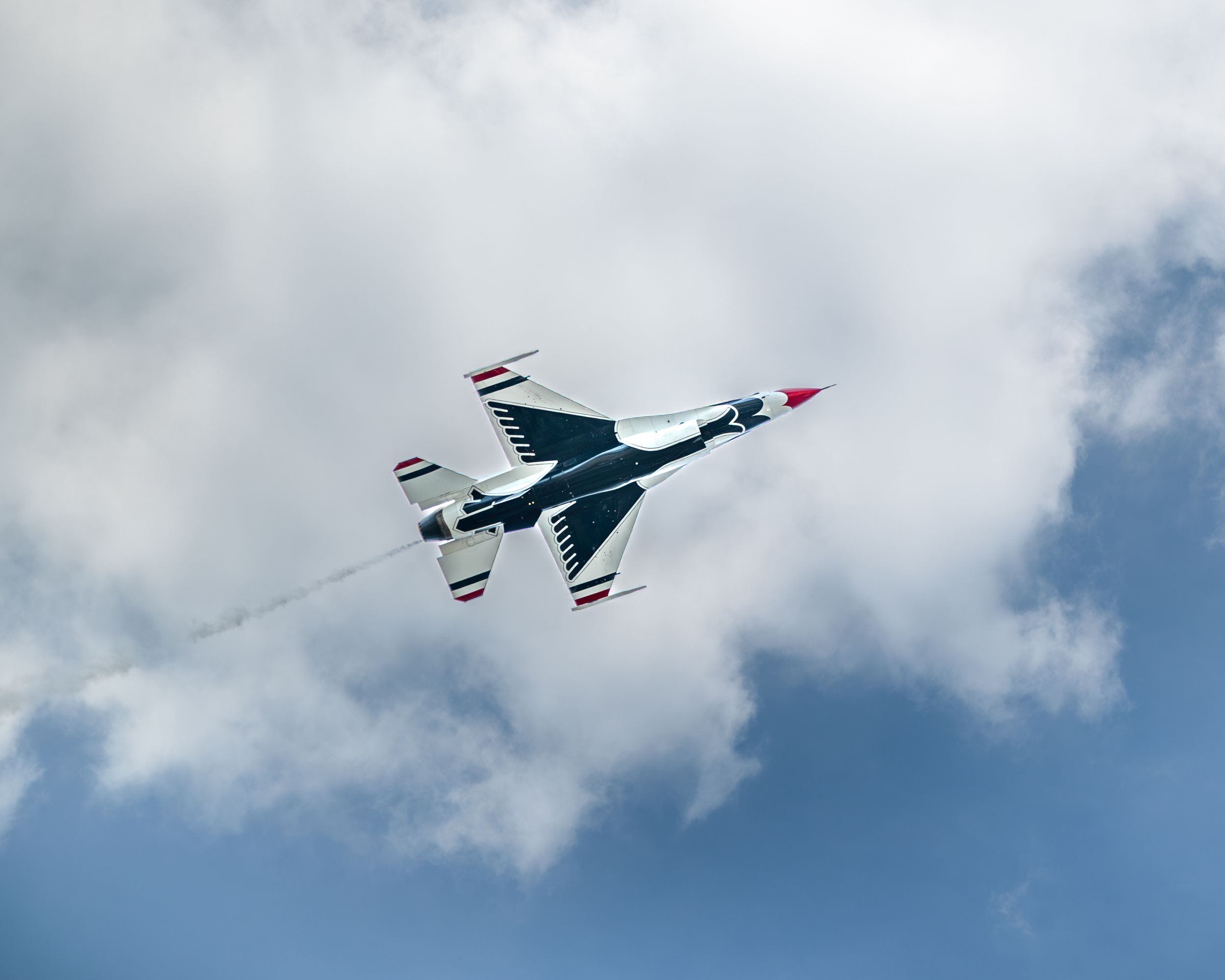 USAF Thunderbirds F-16 jet performing aerial maneuver against cloudy blue sky at airshow.
