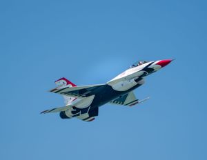 USAF Thunderbirds F-16 fighter jet soaring through clear blue sky during an airshow demonstration.
