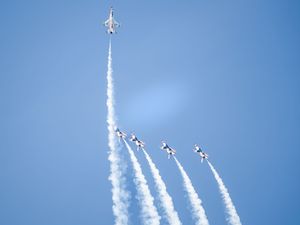 Six US Air Force Thunderbirds jets perform a dramatic formation flight maneuver leaving white smoke trails against a clear blue sky.