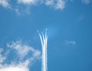 Military jets perform a dramatic aerial maneuver, leaving white smoke trails in a clear blue sky.