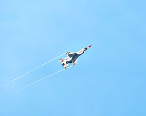 A US Air Force Thunderbirds F-16 jet flies at high speed leaving a white contrail against a clear blue sky.