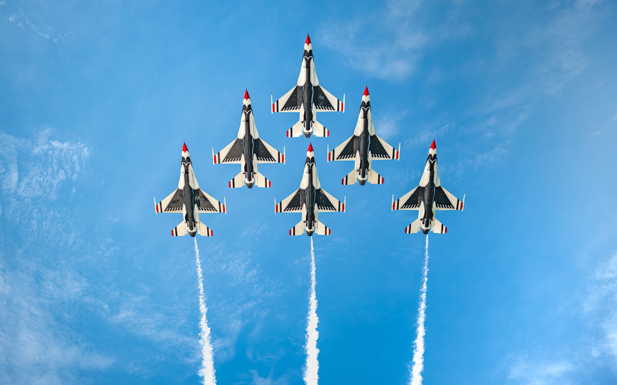 Six U.S. Air Force Thunderbirds jets fly in tight diamond formation against a bright blue sky, trailing white smoke.