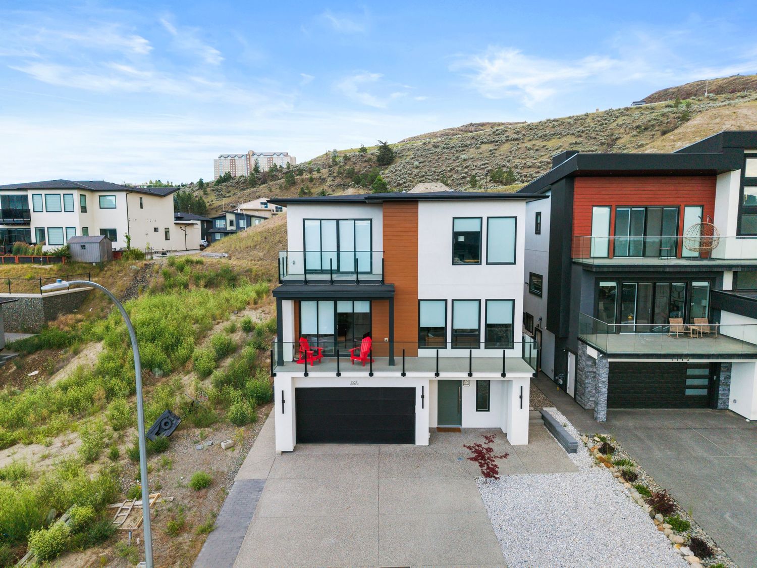 Modern multi-story home with garage, balconies, and hillside backdrop in a contemporary residential neighborhood.