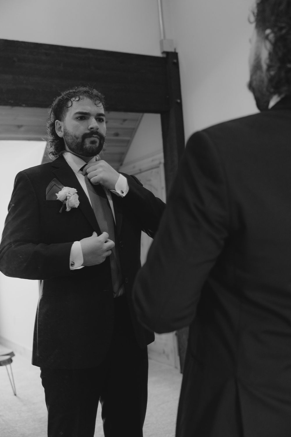 Black and white photo of a groom in a suit getting his tie adjusted before his wedding ceremony.