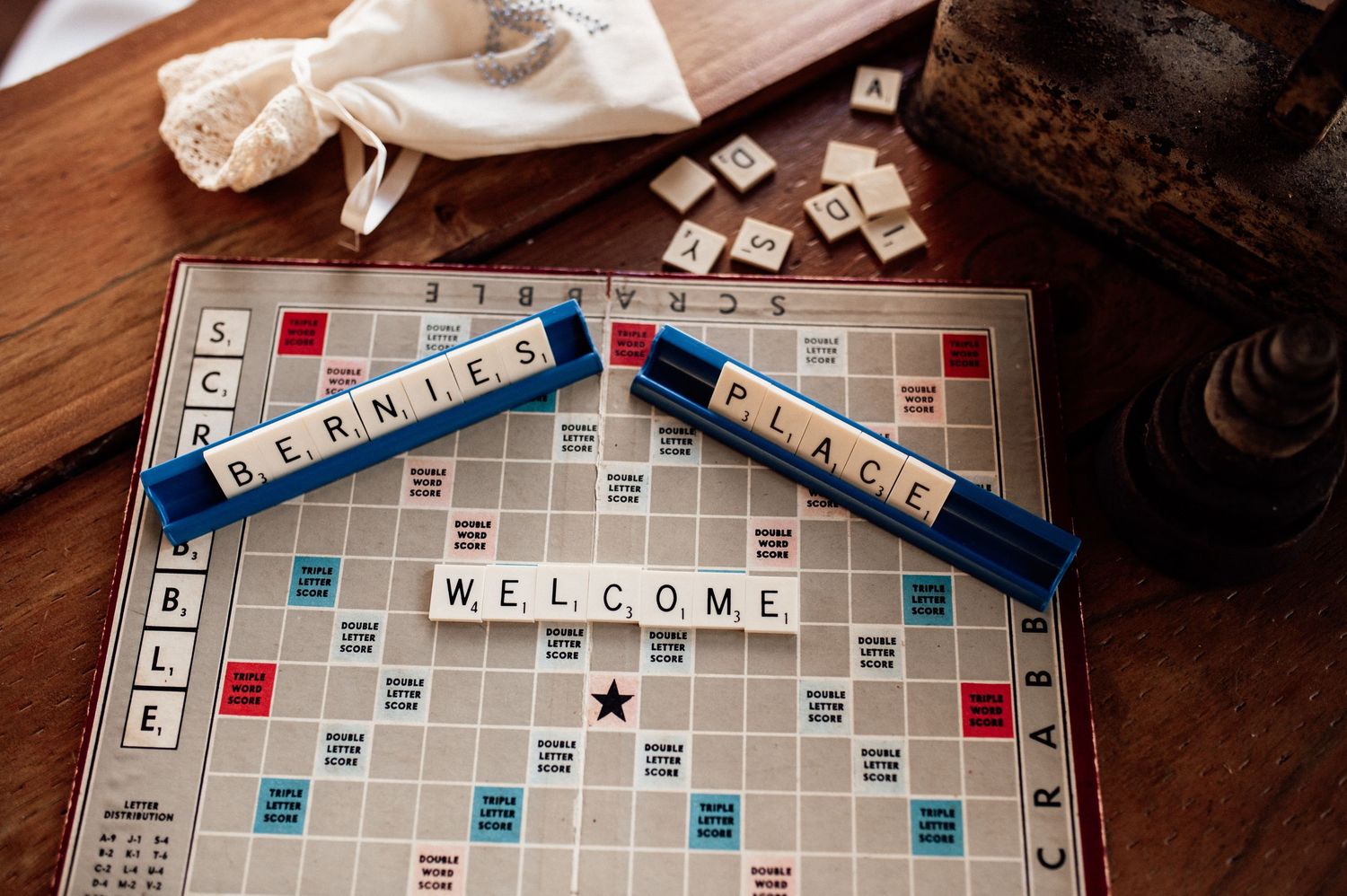 Scrabble board game with tiles spelling WELCOME, BERNIES PLACE on a wooden table.