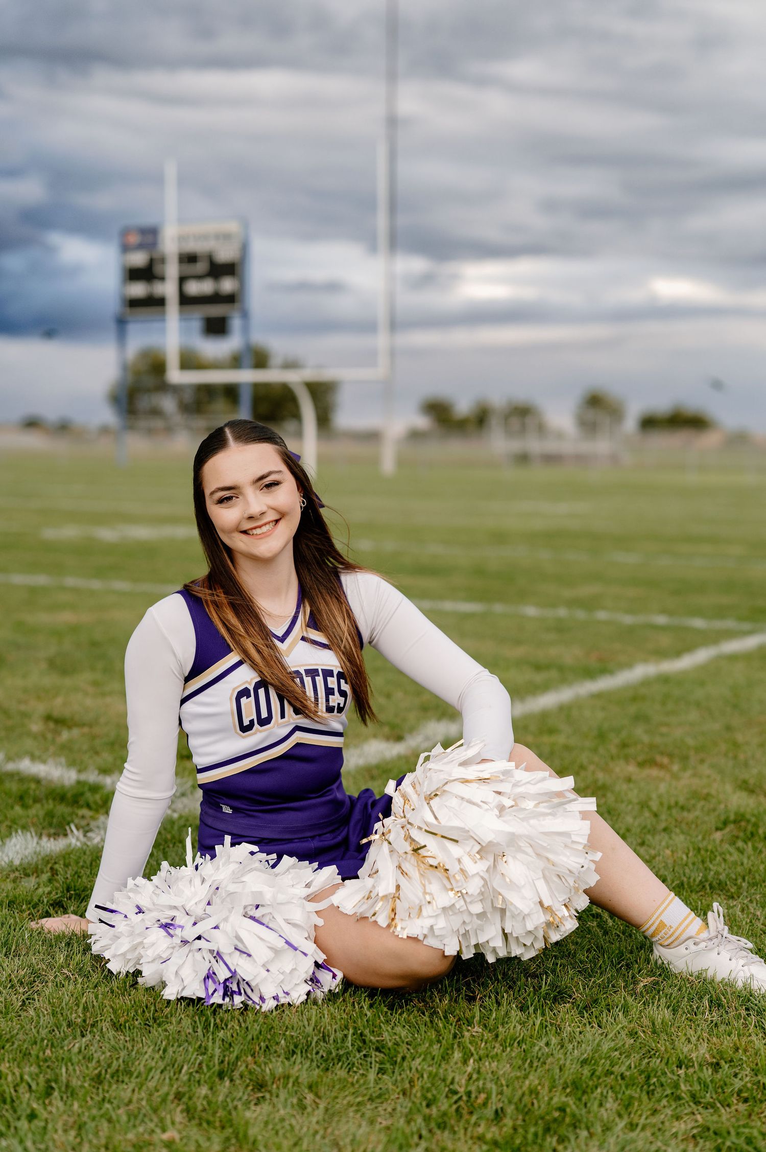 A 2026 senior on her high school football field in her cheer uniform with poms