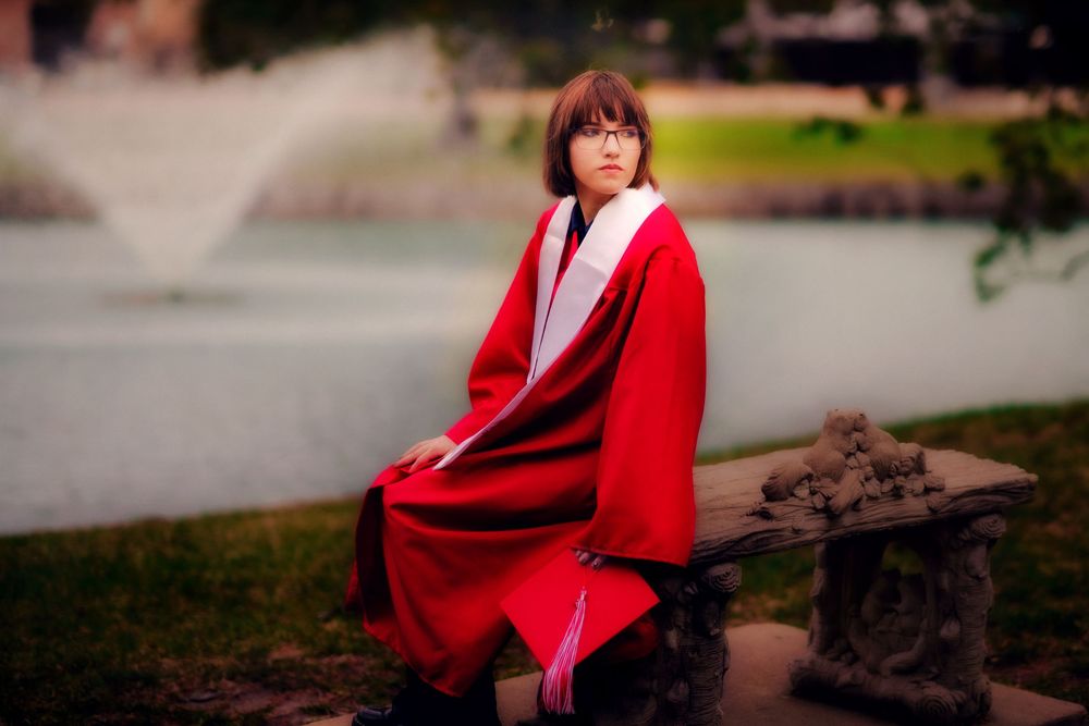 Young woman in red traditional Japanese kimono sitting on stone bench near fountain in park.