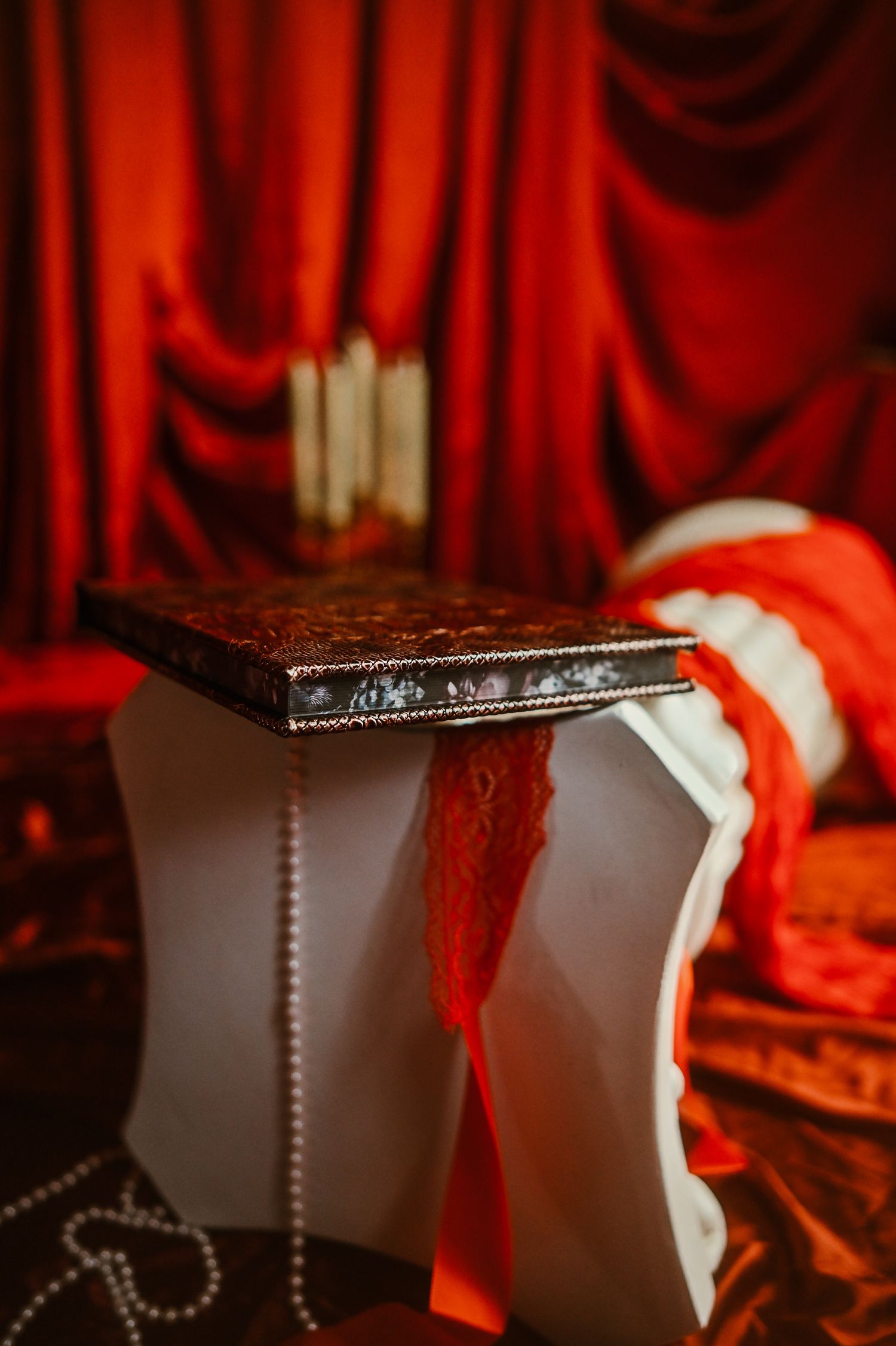 A custom album with floral gilding, sitting on a column in a room of red fabric