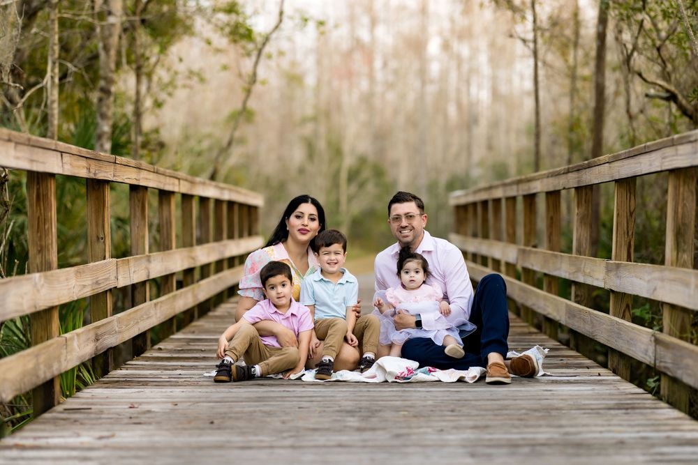 Family of five posing on a wooden bridge surrounded by trees for an outdoor portrait session.