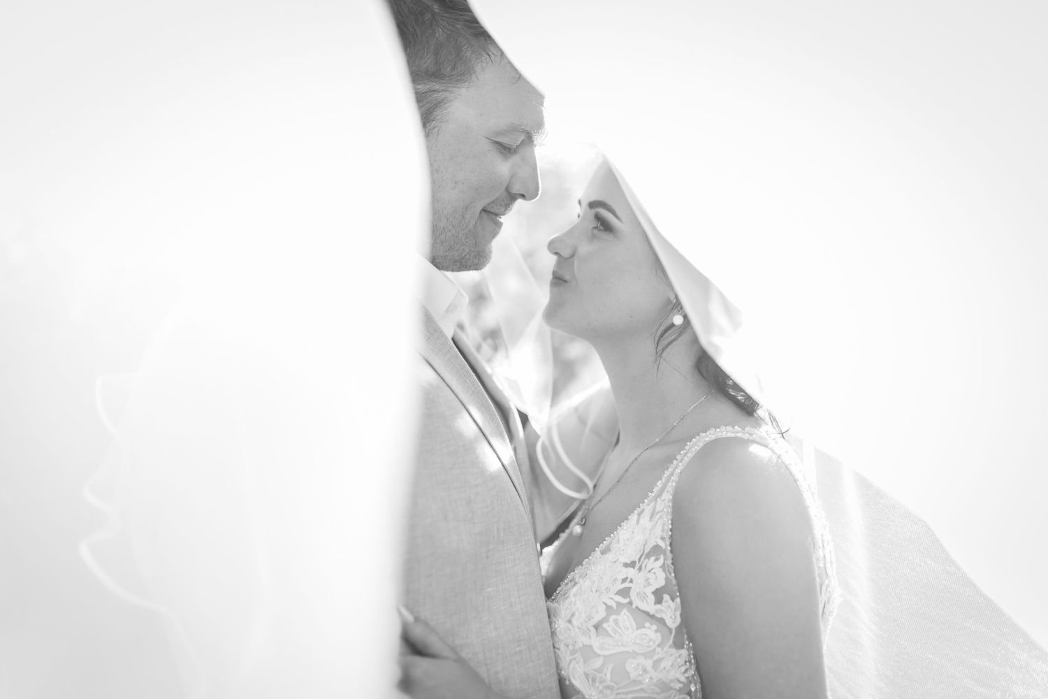 Black and white photo of a bride and groom sharing an intimate moment under a veil on their wedding day.