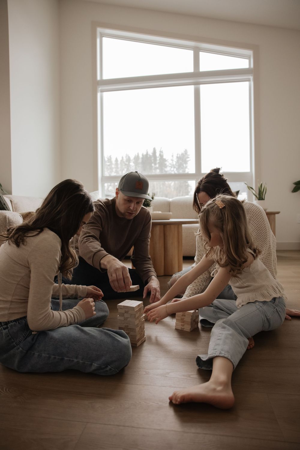 Family sitting on floor playing with wooden blocks together in a bright modern living room.