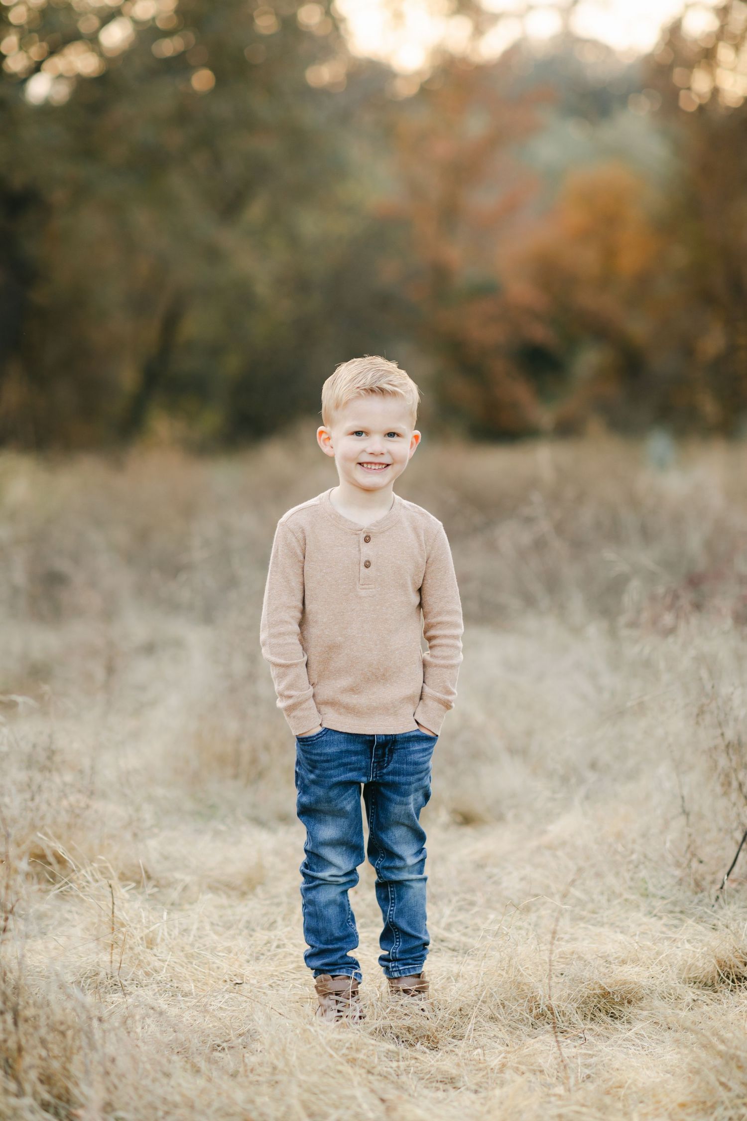 A smiling mother in a teal skirt lifts her happy toddler outdoors in a sunlit autumn field.