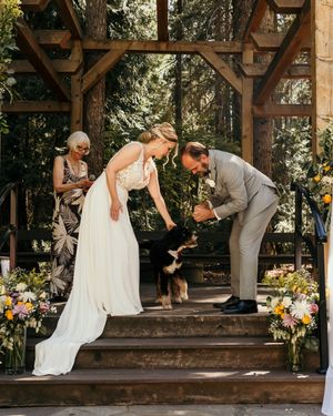 Sweet moment during forest wedding ceremony as couple pets their dog on wooden platform.