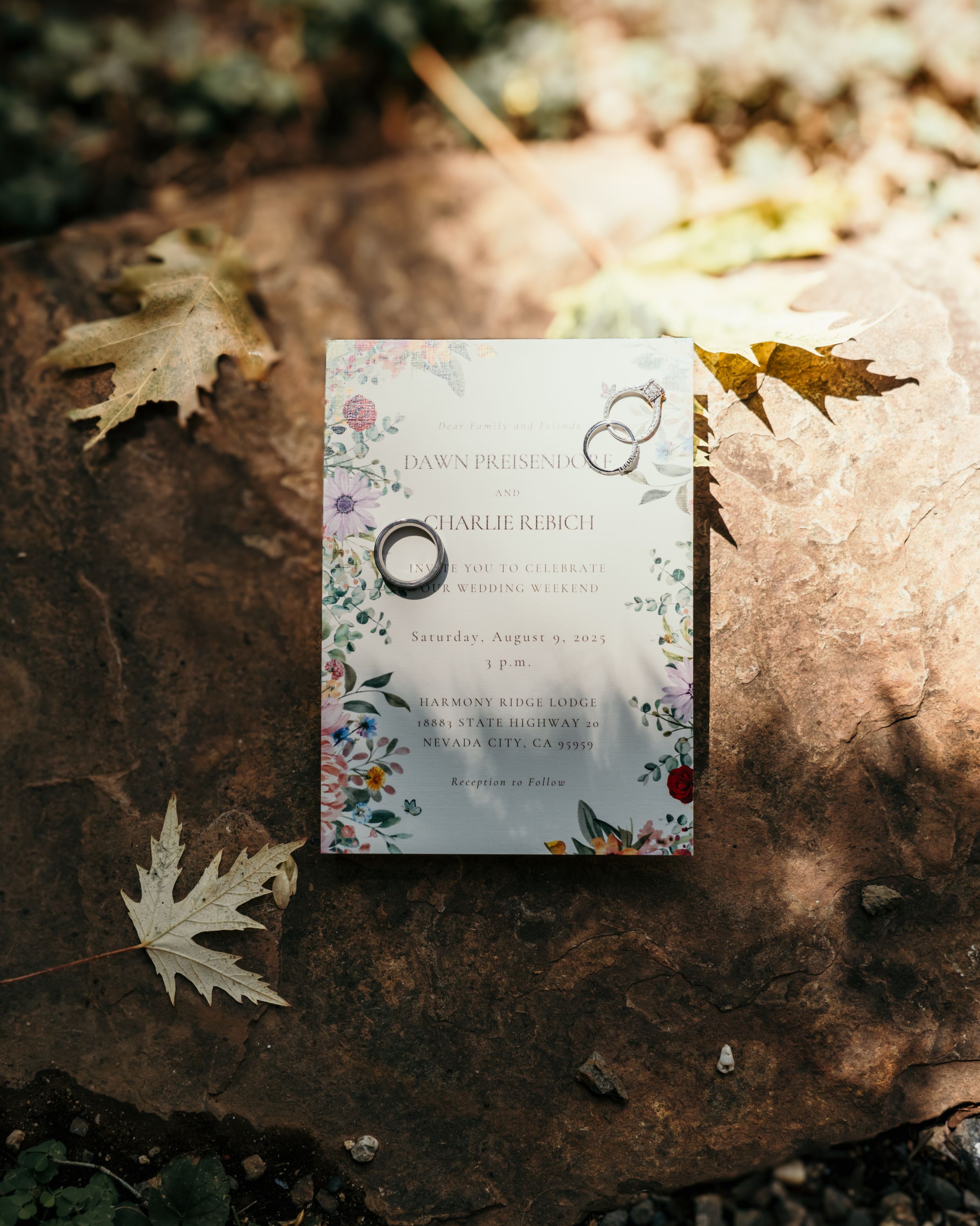 Wedding invitation with delicate floral design lies artistically on ground surrounded by autumn leaves.