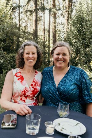 Two wedding guests sharing a laugh while sitting at a table during an outdoor reception.