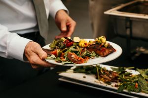 Chef in white uniform plates elegant dishes with colorful garnishes in upscale restaurant kitchen.