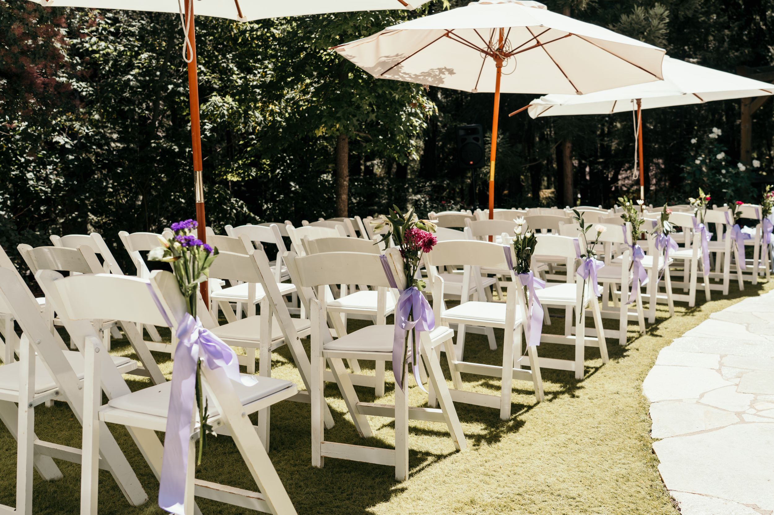White folding chairs and umbrellas arranged outdoors for an elegant garden wedding ceremony.