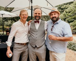 Group of men in formal attire posing together at an outdoor wedding celebration.