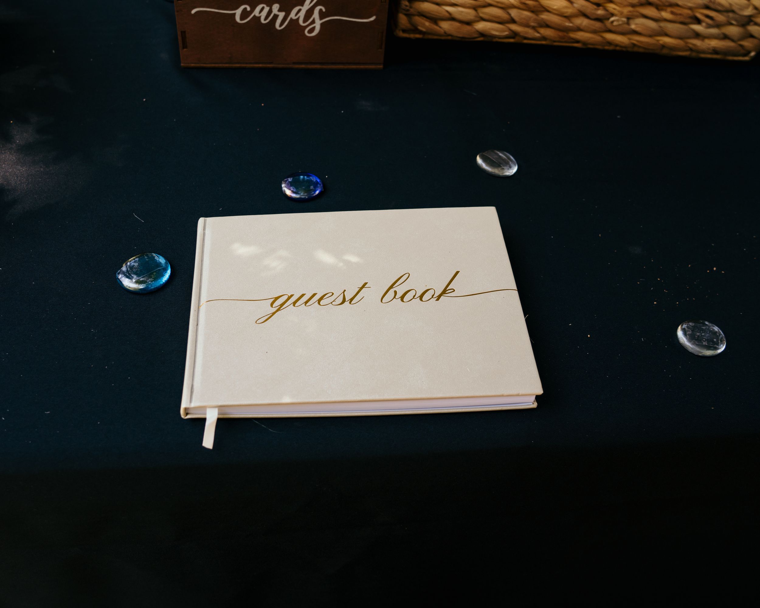 White wedding guest book and cards signs with gold lettering displayed on dark surface with elegant lighting.