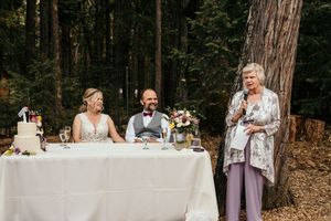 Reception table set up in forest with wedding cake and floral arrangements.