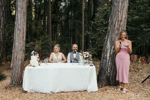 A wedding reception setup in a wooded forest area with tables and decor among tall trees.