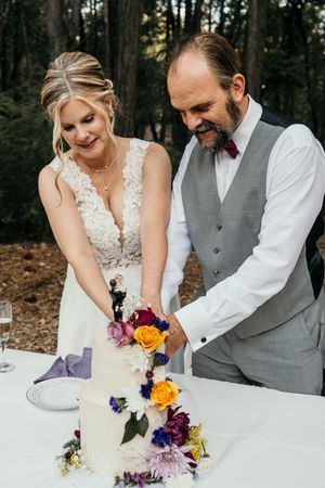 Couple cutting their wedding cake decorated with vibrant purple and orange flowers.