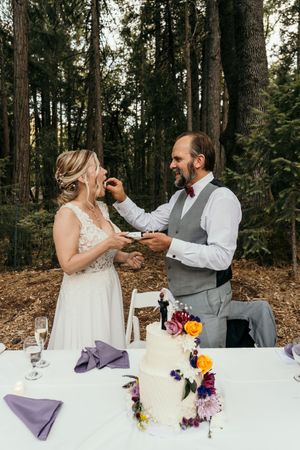 A couple shares a toast during their wedding reception at an outdoor forest venue with purple decor.