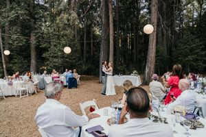 Outdoor forest wedding reception with string lights and white tables set among tall trees.