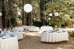 Outdoor wedding reception tables set with white linens and blue accents in a wooded forest setting.
