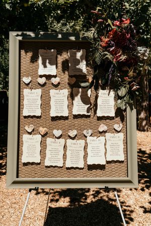Wedding seating chart displayed on rustic wire mesh frame with decorative paper hearts.