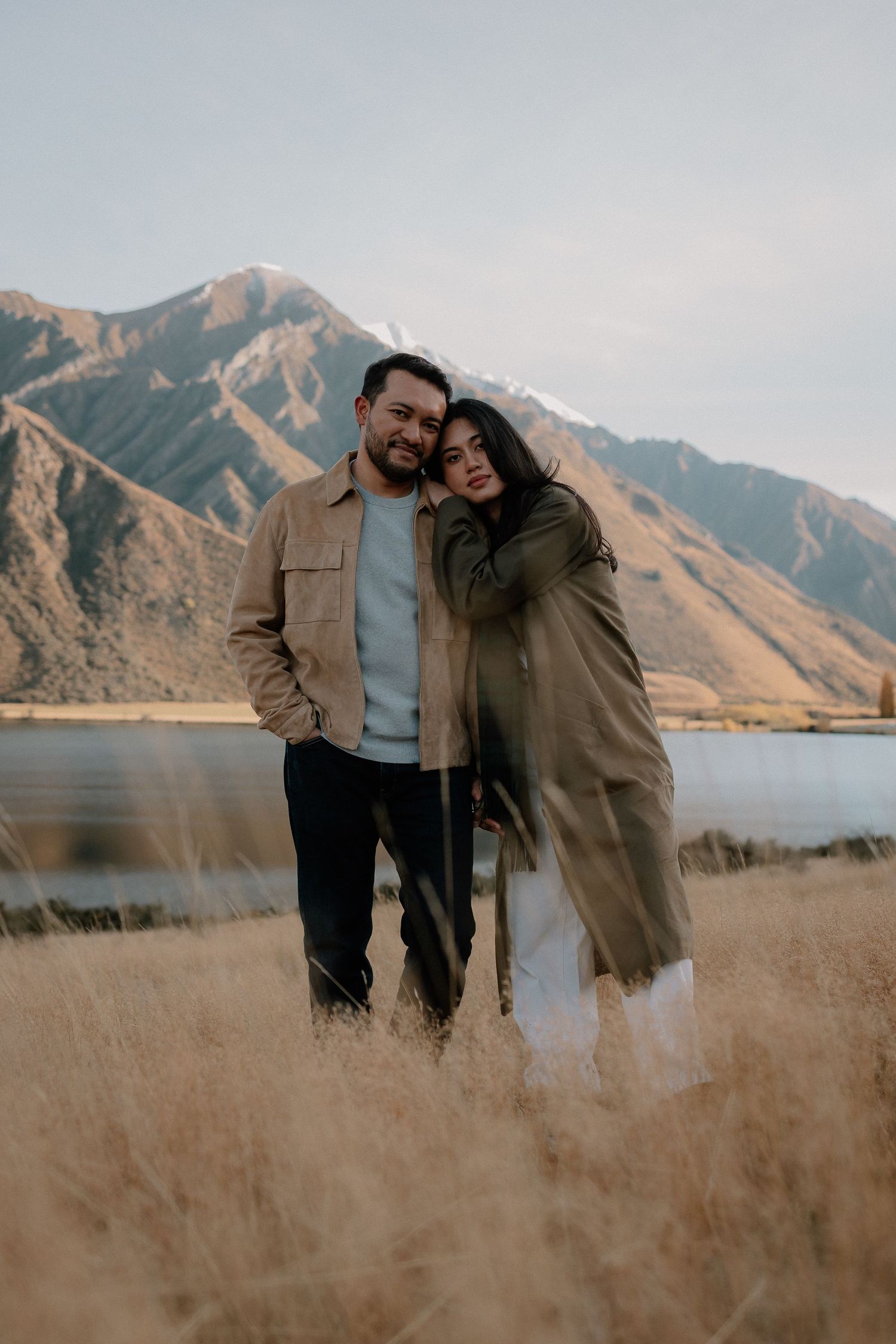 Couple embracing in golden field with mountain lake backdrop in autumn.