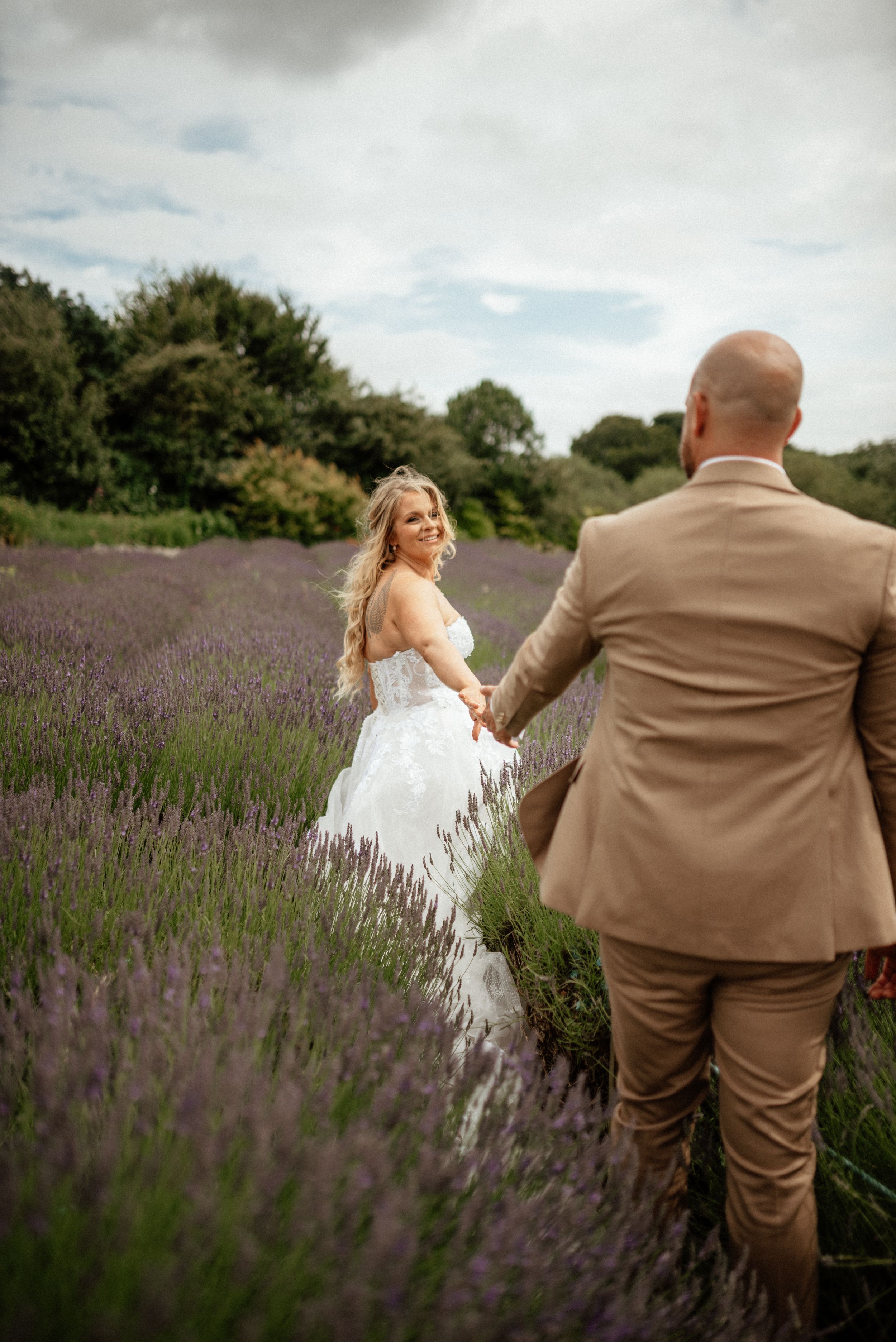 Couple in wedding attire poses playfully in blooming lavender field.