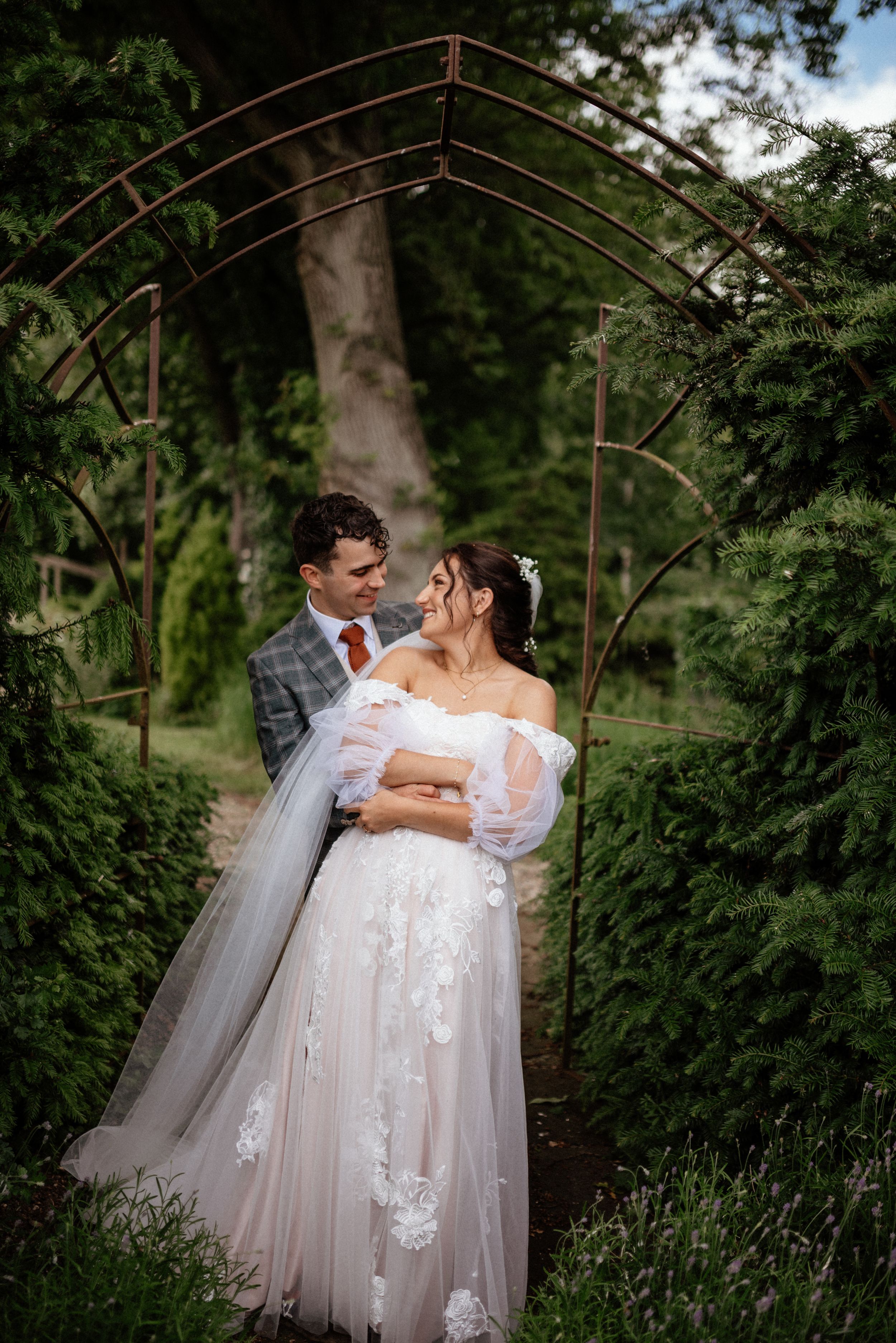 Wedding couple embraces under garden archway surrounded by lush greenery.