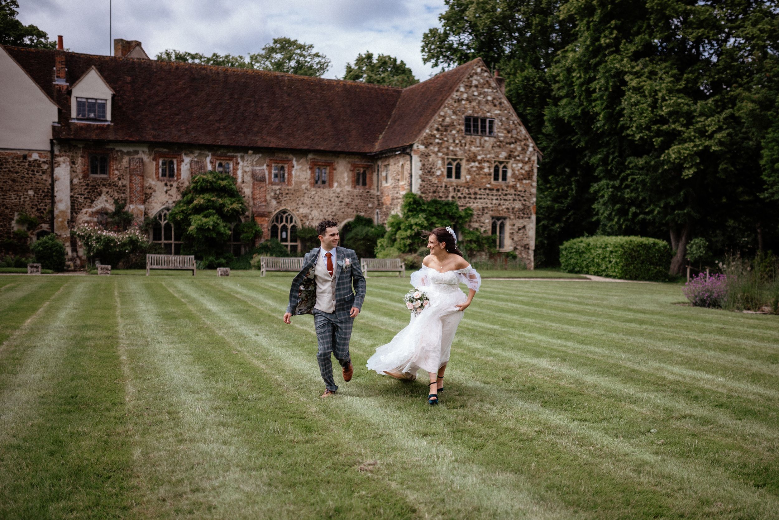 Newlyweds walking on manicured lawn with historic stone building in background.