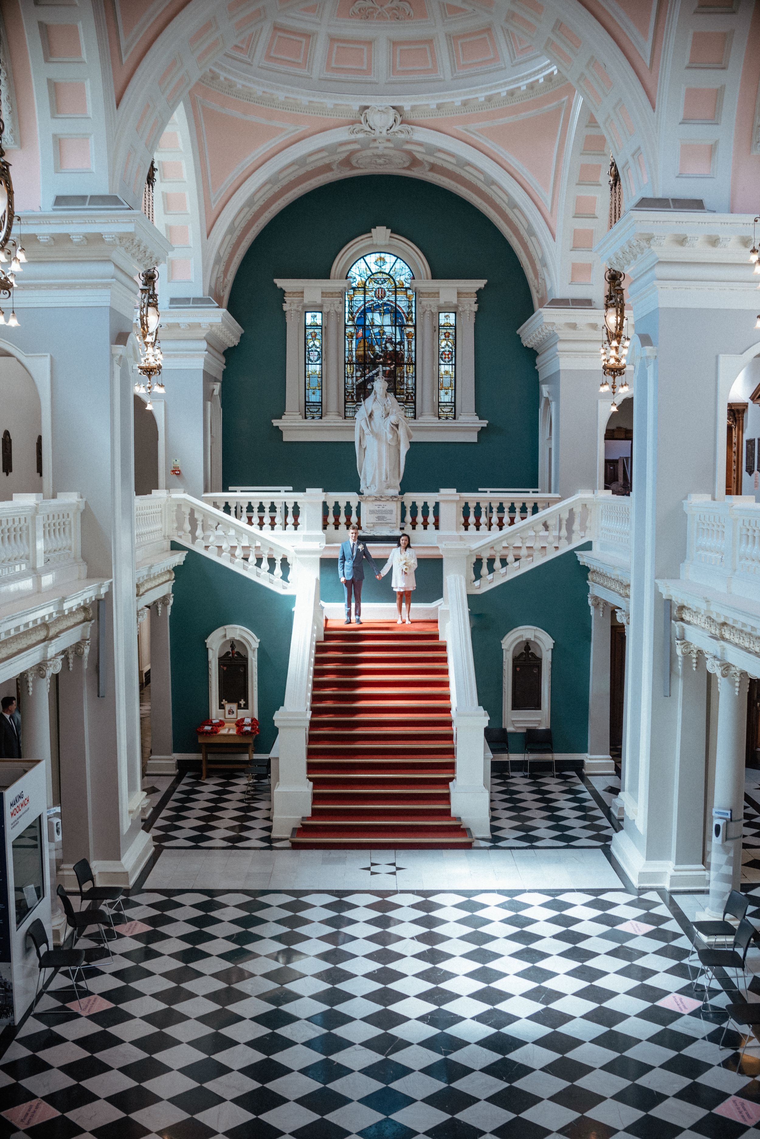 Grand interior hallway with black and white checkered floor, red carpeted stairs, and ornate white architectural details.
