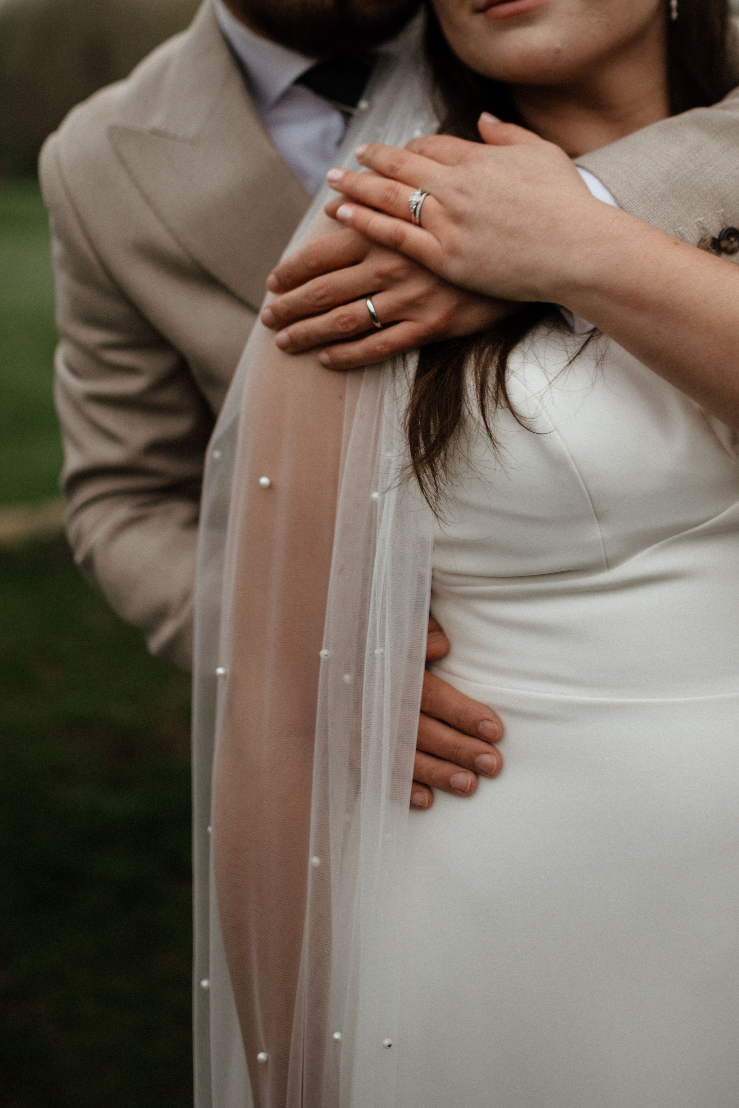 Close-up romantic wedding photo showing couple embracing in beige suit and white dress with delicate veil details.