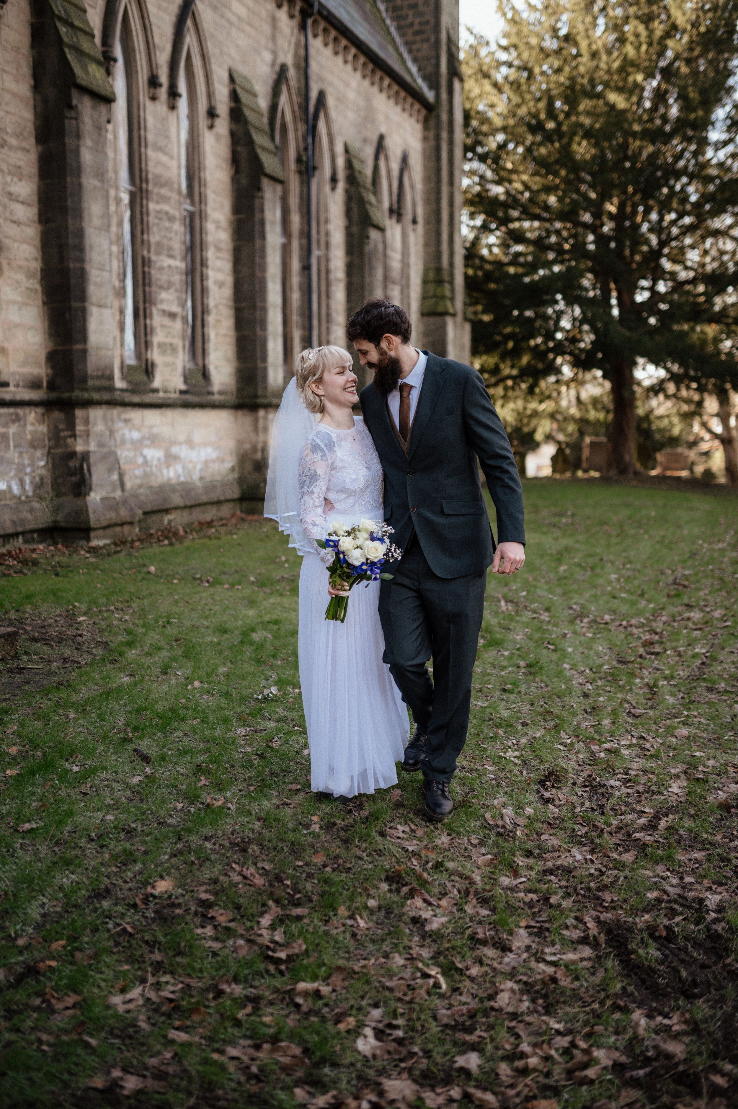 A couple shares a romantic moment outside a historic stone church with gothic architecture on their wedding day.
