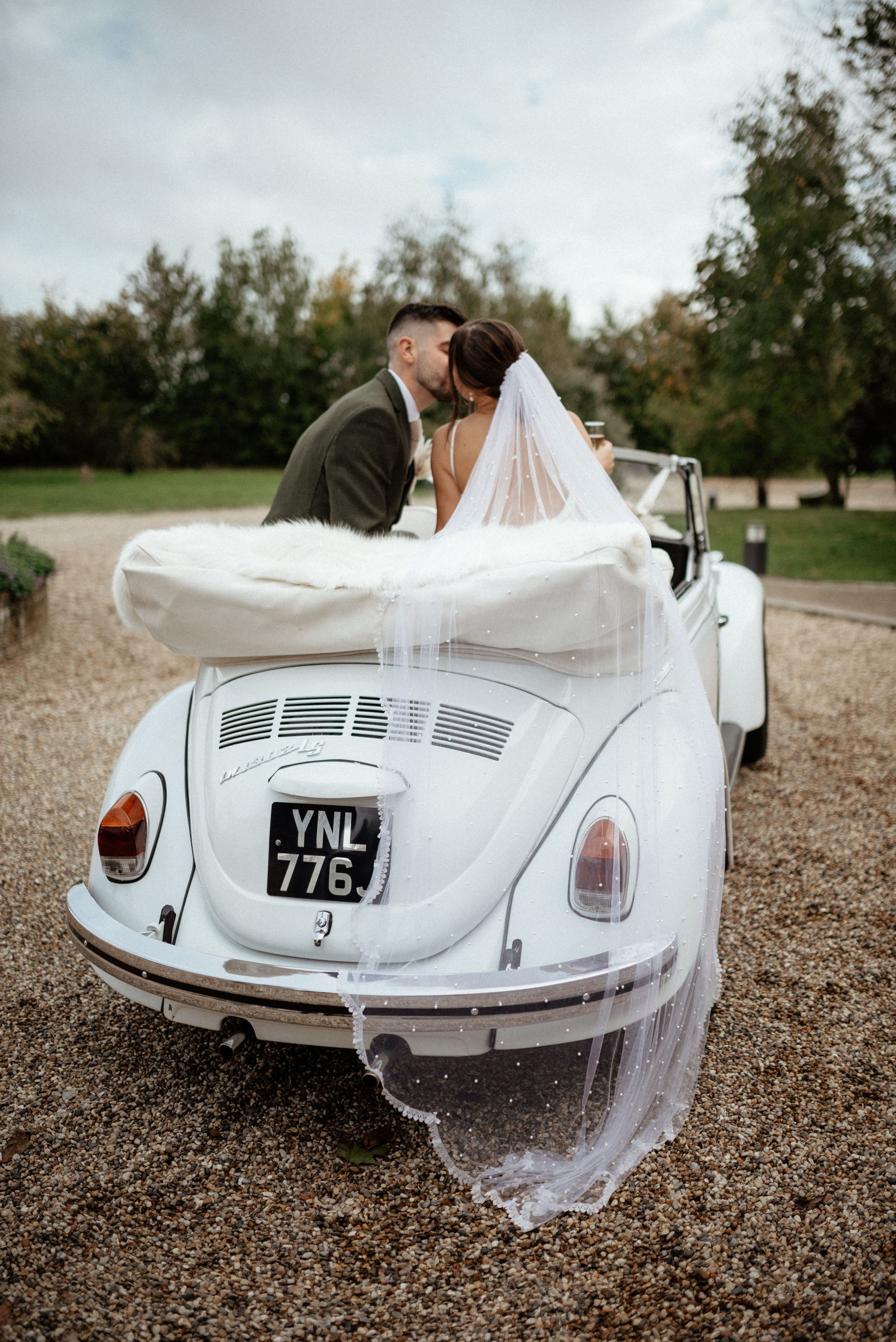 Classic white Volkswagen Beetle convertible with flowing bridal veil at a wedding.