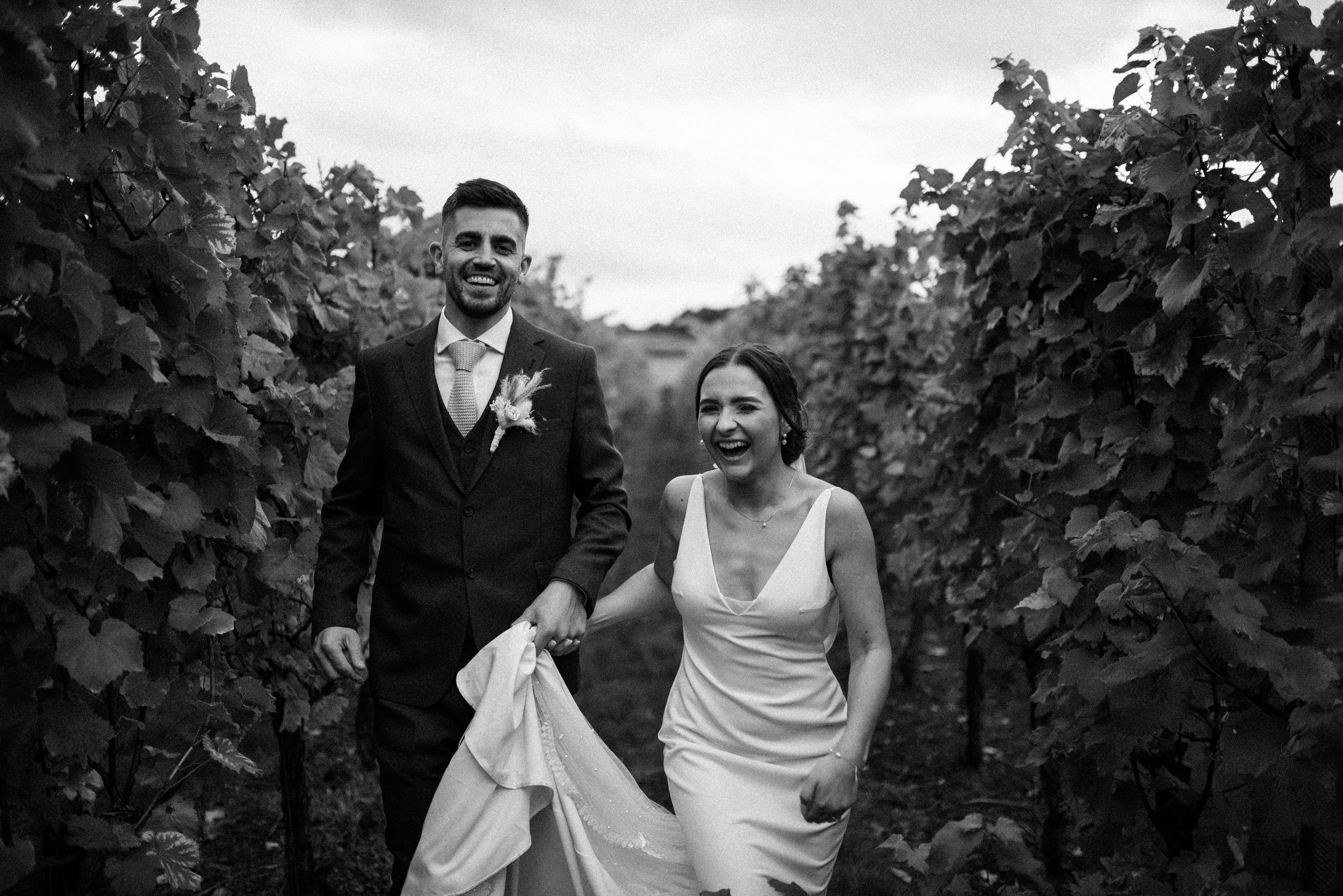 Couple dancing and laughing together in a lush green vineyard setting.