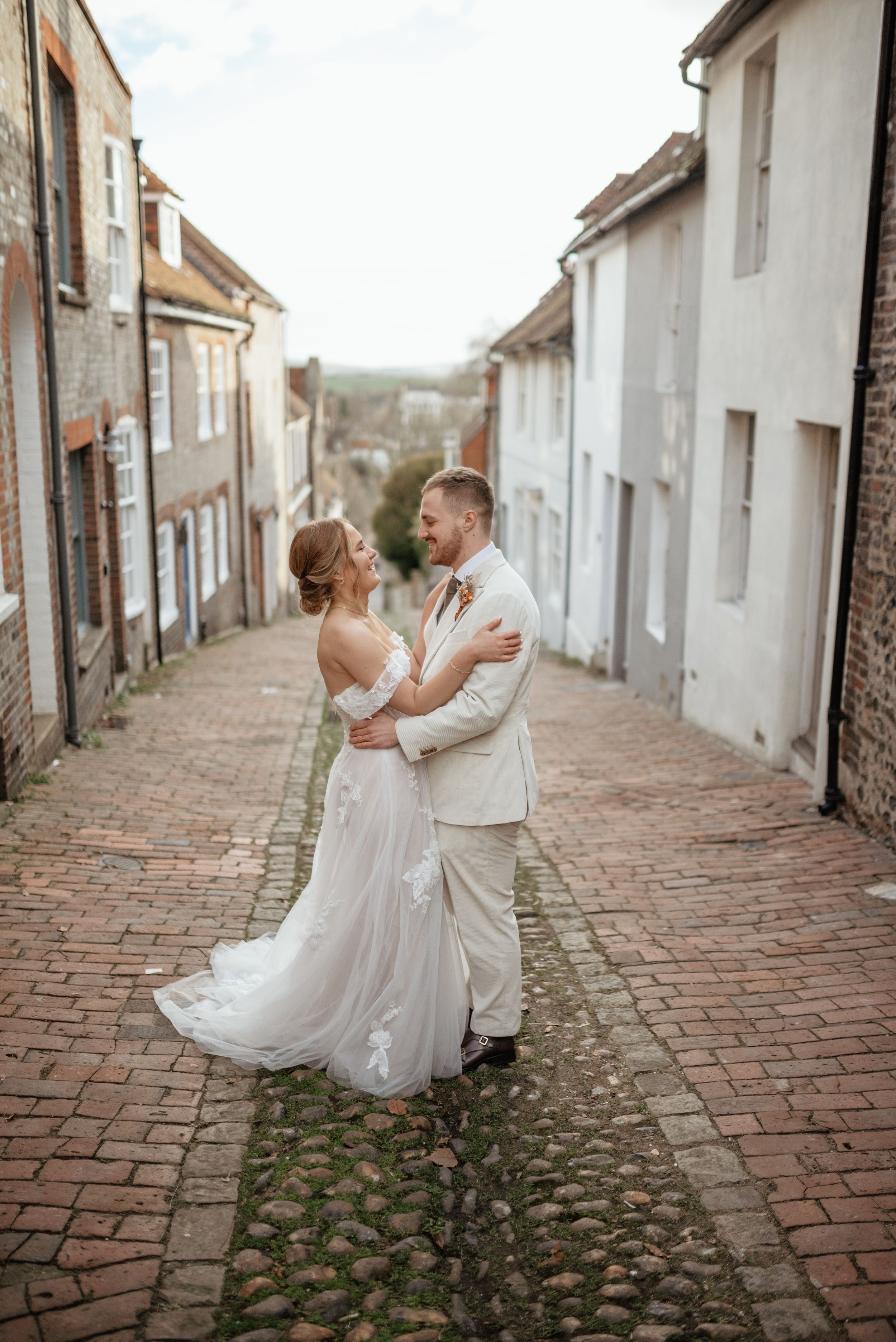Newlyweds dancing on a charming cobblestone street between historic buildings.