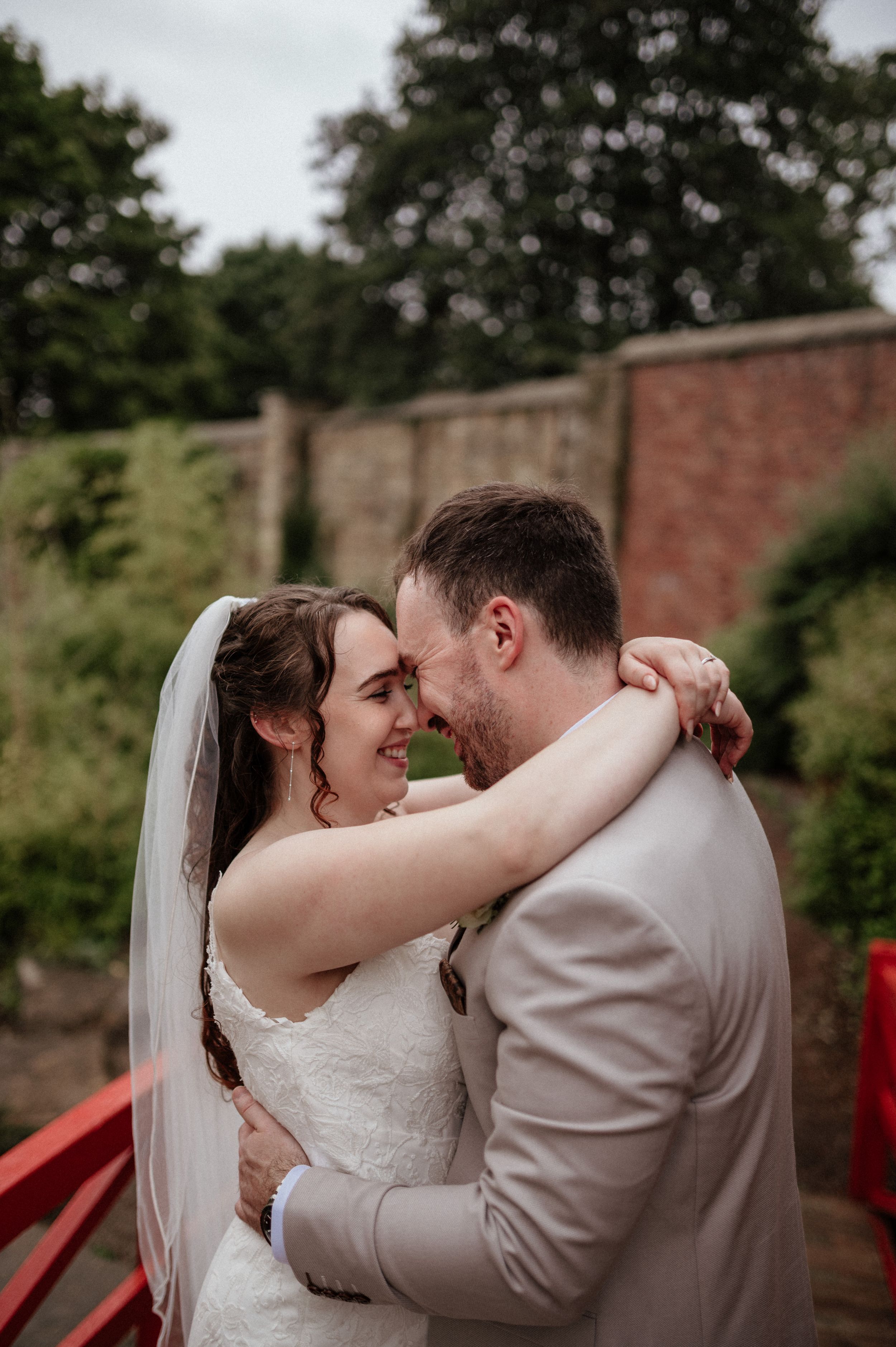 Intimate wedding couple embraces against rustic brick wall backdrop.