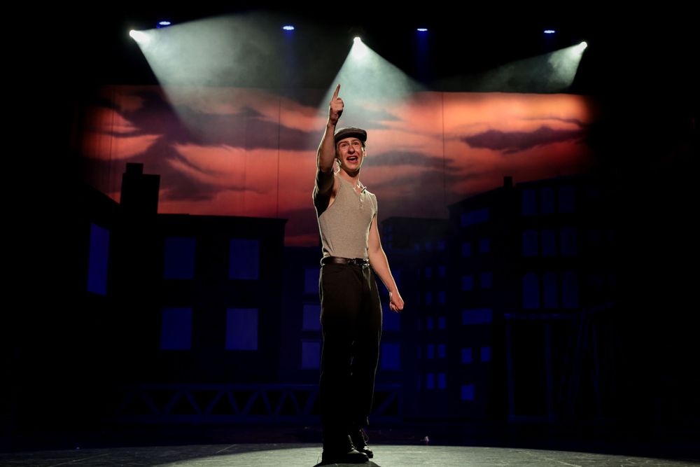Solo performer on stage with dramatic lighting and sunset backdrop.