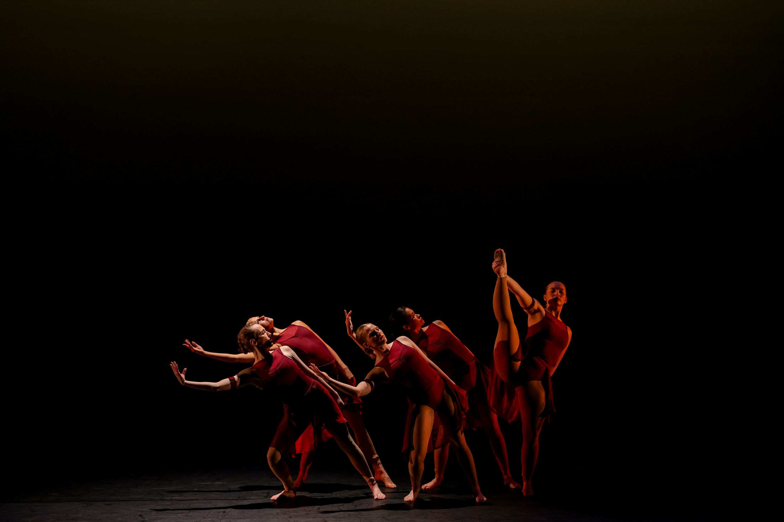 A dramatic modern dance performance sequence showing dancers in red costumes moving across a dark stage. Theatre photography.