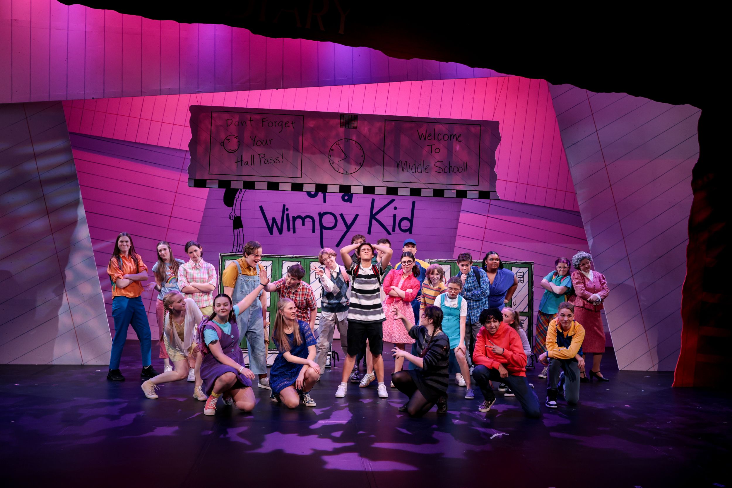 Musical theater performers strike dynamic poses on stage during a colorful production of Diary of a Wimpy Kid.